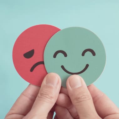 the hand keeping a sad and happy paper face
